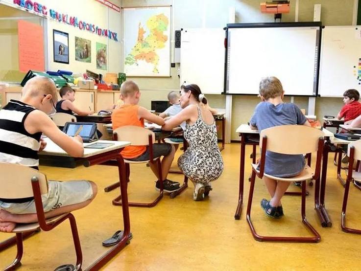 Unterricht im Klassenraum mit Blick von den hinteren Reihen nach vorn zur Tafel - schreibende Schulkinder