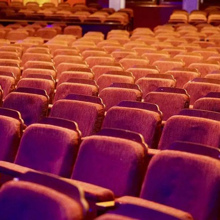 Bildausschnitt rot gepolsterter Theaterstuhlreihen in etwas abgedunkeltem, künstlichem Licht