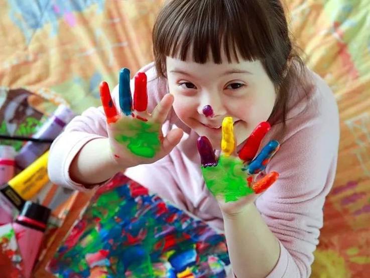 Mädchen lächelt aufblickend in die Kamera und zeigt gut gelaunt ihre mit Fingerfarben eingefärbten Handflächen